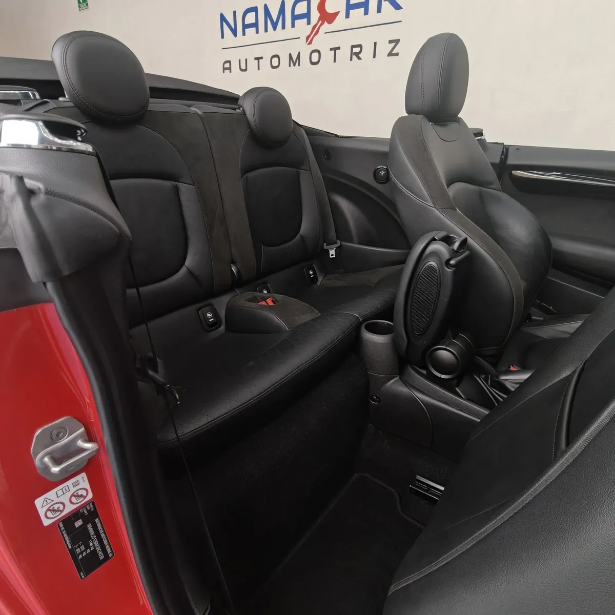 Vista lateral izquierda trasera de la segunda fila de asientos de piel negros en un Mini Cooper S Convertible Hot Chili 2021 seminuevo con capota abierta en Namacar Automotriz.
