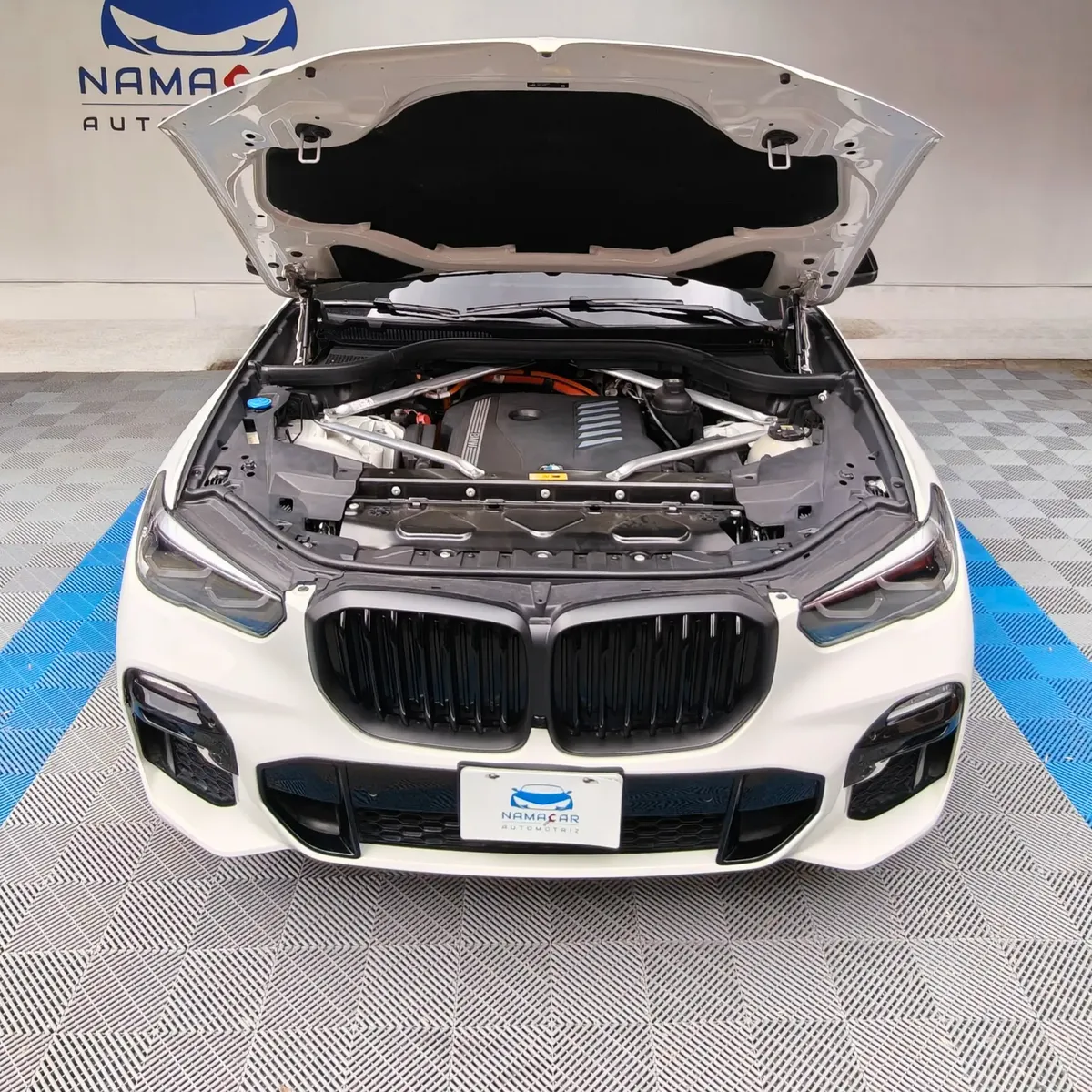 Vista exterior frontal con el cofre abierto que muestra el motor de una SUV híbrida premium BMW X5 2021 seminueva en color blanco, en Namacar Automotriz.