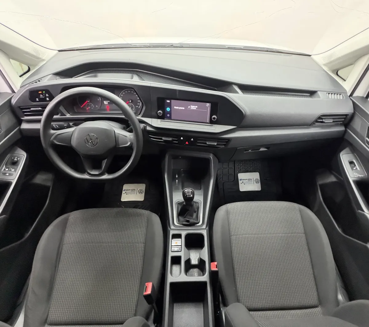 Vista interior cenital desde arriba que muestra la cabina con tablero, volante, asientos de tela y palanca de transmisión manual de una camioneta pick-up Volkswagen Saveiro 1.6 Robust 2025 seminueva en color blanco.
