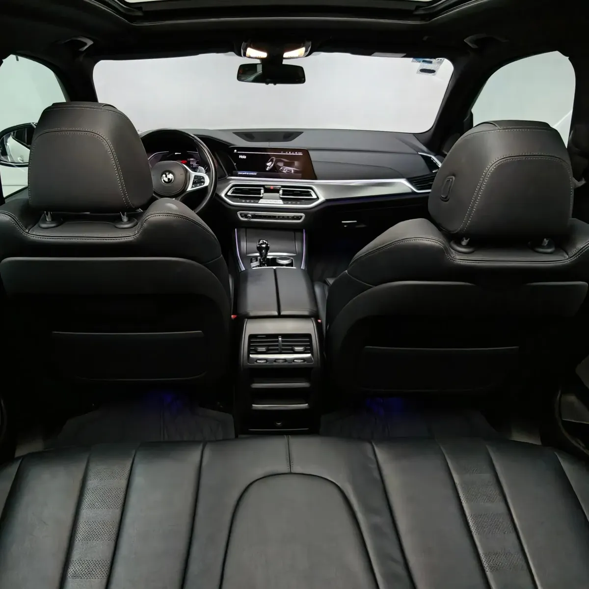 Vista interior en perspectiva trasera central desde la segunda fila que muestra los respaldos delanteros, la consola central trasera y el tablero digital de una SUV premium BMW X5 2021 seminueva con asientos de piel oscuros.