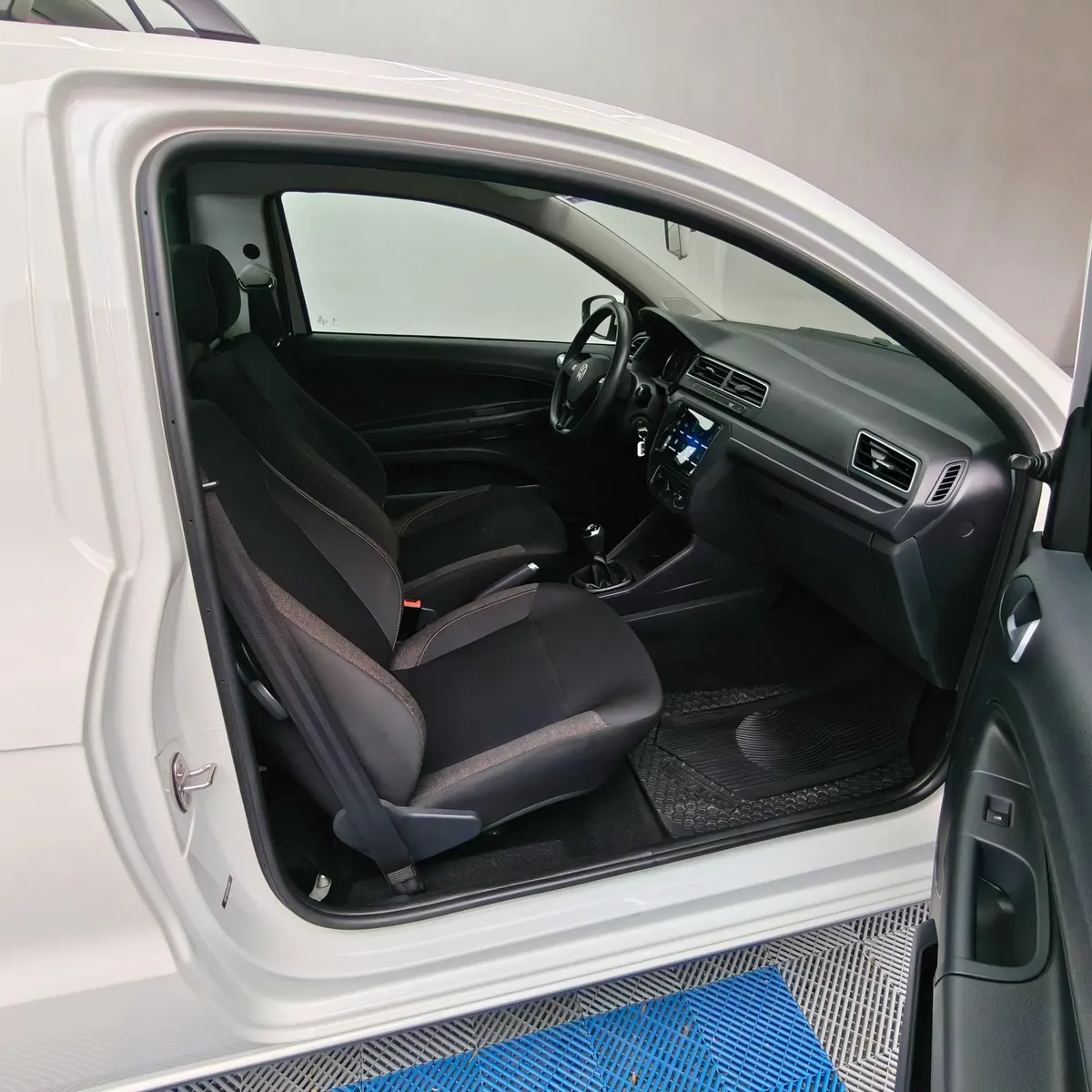 Vista interior desde la puerta del copiloto abierta que muestra los asientos de tela oscuros, el tablero y el volante de una camioneta pick-up Volkswagen Saveiro 1.6 Robust MT año 2025 seminueva en ángulo oblicuo derecho.