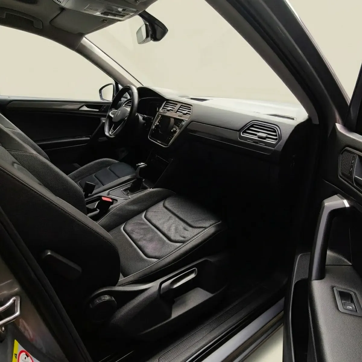 Vista interior desde la puerta del pasajero abierta que muestra la primera fila de asientos deportivos en piel y el tablero ergonómico de una SUV Volkswagen Tiguan 1.4 R-Line 2022 seminueva en ángulo oblicuo derecho.