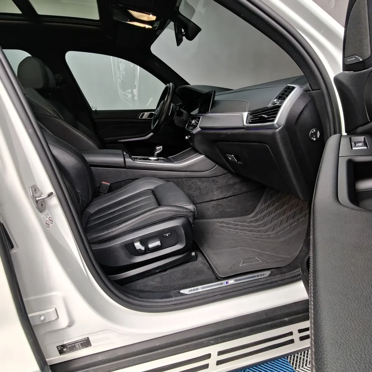 Vista interior desde la puerta del copiloto abierta que muestra el asiento de piel del pasajero delantero, los tapetes texturizados y el tablero de una SUV de lujo BMW X5 2021 seminueva en ángulo oblicuo derecho.