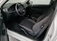 Vista interior desde la puerta del conductor abierta que muestra el asiento de tela del piloto, el volante y el tablero de una camioneta pick-up Volkswagen Saveiro 1.6 Robust MT año 2025 seminueva en ángulo oblicuo izquierdo.