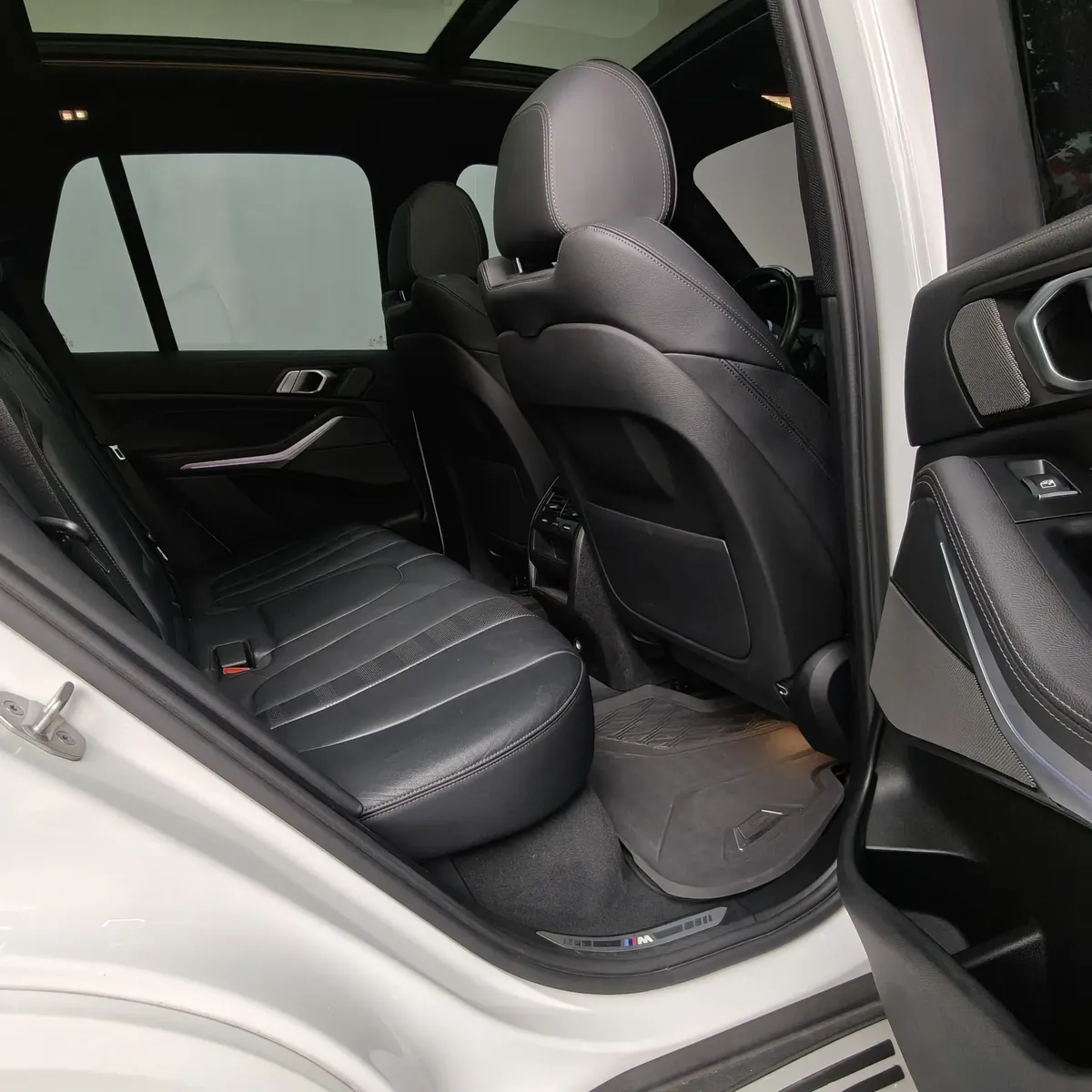 Vista interior desde la puerta trasera derecha abierta que muestra los asientos de piel de la segunda fila, el respaldo del copiloto y el techo panorámico de una SUV premium BMW X5 2021 seminueva en ángulo oblicuo derecho.