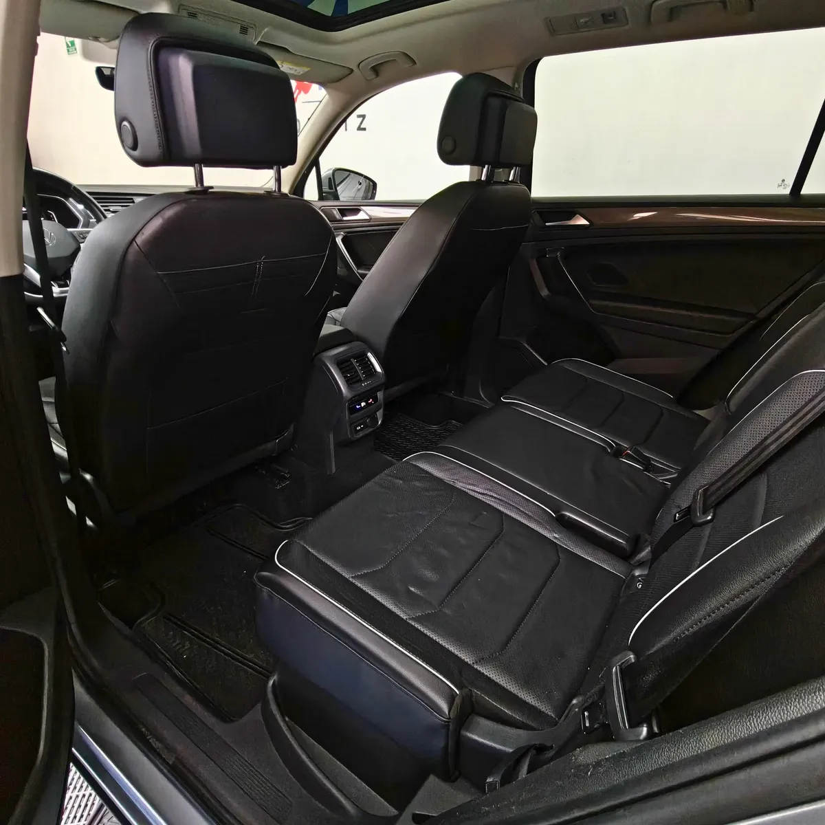 Vista interior desde la puerta trasera izquierda abierta que muestra la segunda fila de asientos en piel, el espacio posterior para pasajeros y los respaldos delanteros de una SUV Volkswagen Tiguan 1.4 R-Line 2022 seminueva en ángulo oblicuo izquierdo.