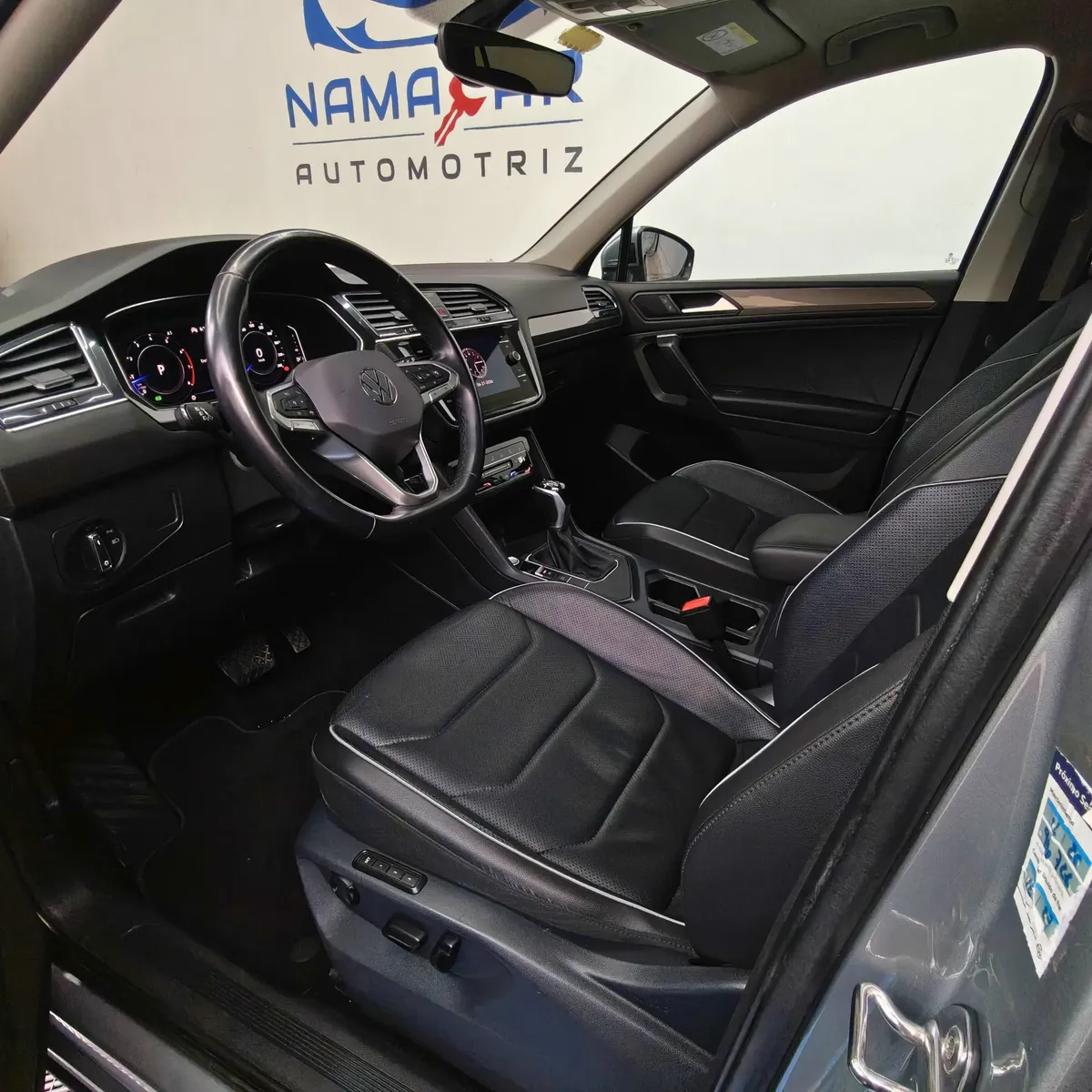 Vista interior desde la puerta del conductor abierta que muestra el asiento de piel del piloto, el volante multifunción y el tablero digital de una SUV Volkswagen Tiguan 1.4 R-Line 2022 seminueva en ángulo oblicuo izquierdo.