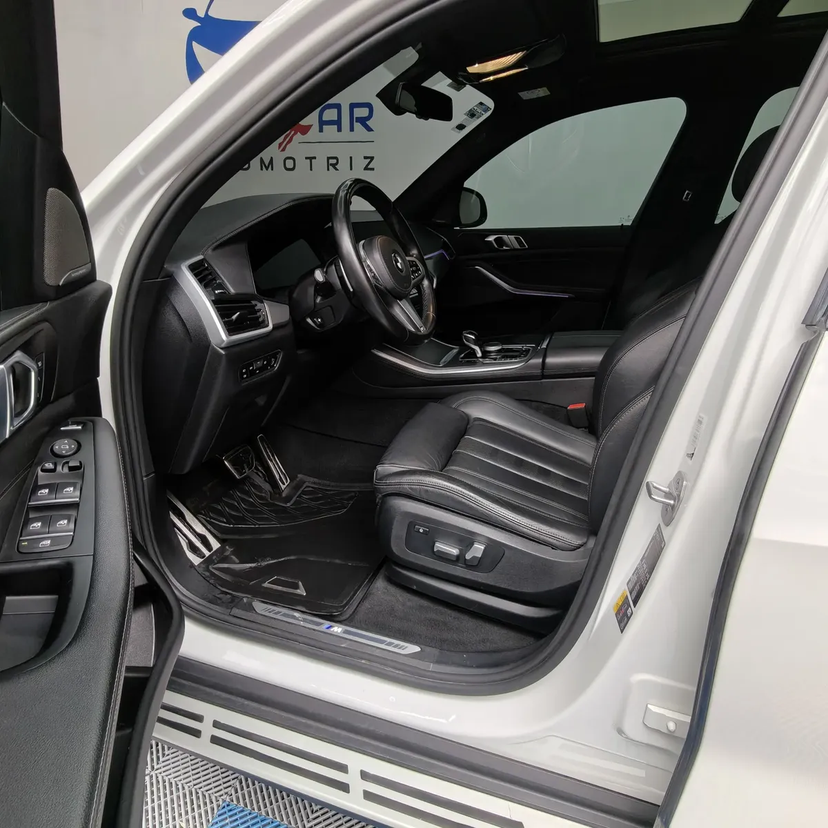 Vista interior desde la puerta del conductor abierta que muestra el asiento de piel del piloto, el volante multifunción y el tablero de una SUV de lujo BMW X5 2021 seminueva en ángulo oblicuo izquierdo.