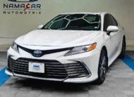 Auto sedán híbrido Toyota Camry 2.5 HEV XLE año 2024 seminuevo en color blanco, vista exterior frontal en ángulo de tres cuartos izquierda exhibido en Namacar Automotriz.