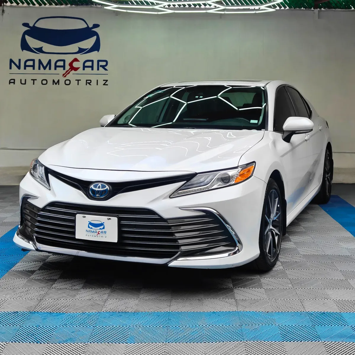 Auto sedán híbrido Toyota Camry 2.5 HEV XLE año 2024 seminuevo en color blanco, vista exterior frontal en ángulo de tres cuartos izquierda exhibido en Namacar Automotriz.