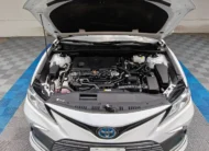 Vista exterior frontal en picada superior con el cofre abierto que muestra el motor 2.5 L híbrido de un auto sedán Toyota Camry 2.5 HEV XLE año 2024 seminuevo en color blanco, en Namacar Automotriz.