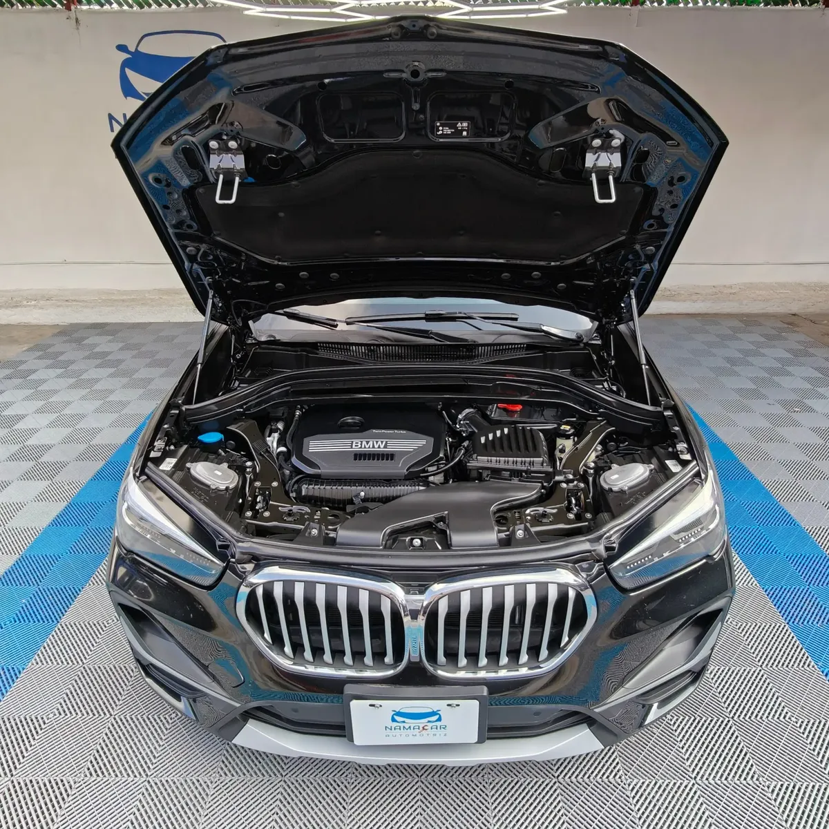 Camioneta SUV de lujo BMW X1 2.0 sDrive20i sDrive 20iA X Line transmisión automática año 2022 seminueva en color negro, vista exterior frontal centrada con el cofre abierto exhibiendo el compartimento del motor TwinPower Turbo 2.0 L en Namacar Automotriz.