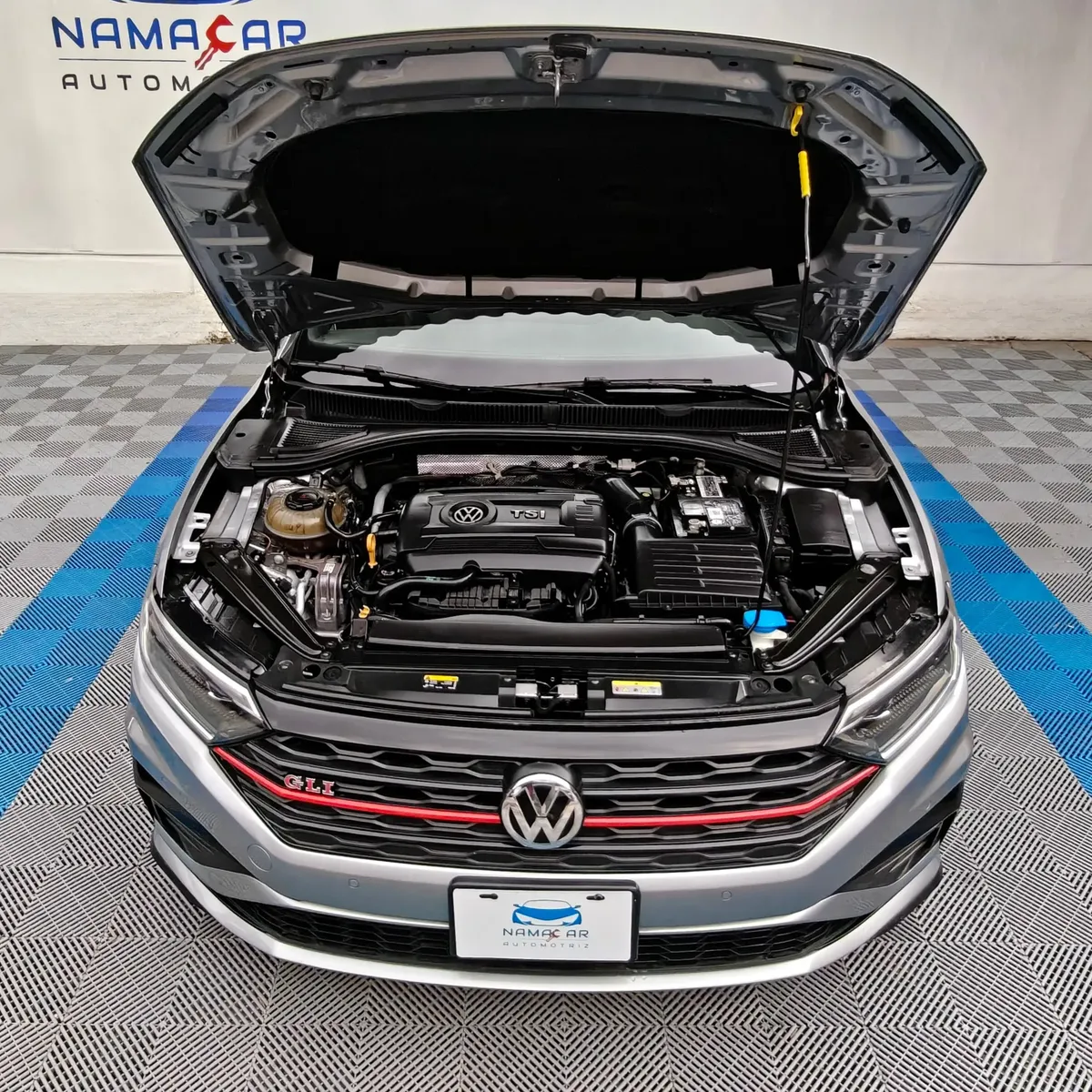 Vista exterior frontal en picada superior con el cofre abierto que muestra el motor 2.0 Turbo de un auto sedán deportivo Volkswagen Jetta 2.0 GLI DSG automático año 2021 seminuevo en color gris plata, en Namacar Automotriz.