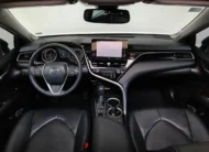 Vista interior cenital desde arriba que muestra la cabina, el tablero, la pantalla multimedia flotante, el volante multifunción y los asientos delanteros en piel negra de un auto sedán híbrido Toyota Camry 2.5 HEV XLE año 2024 seminuevo.