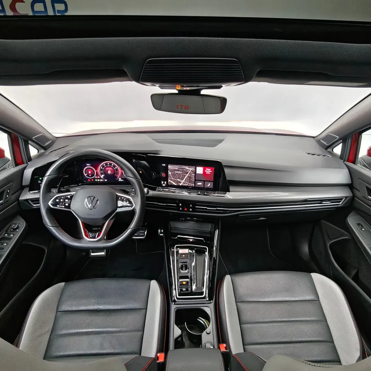 Vista interior desde los asientos traseros hacia el frente que muestra el tablero Digital Cockpit, la pantalla de infoentretenimiento, el volante deportivo, la consola central y los asientos delanteros de un hatchback deportivo Volkswagen Golf GTI 2.0 241 HP DSG7 año 2024 seminuevo.