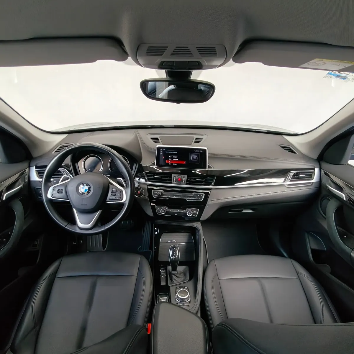 Vista interior panóramica desde los asientos traseros que muestra la cabina delantera completa, el tablero de instrumentos, la pantalla de infoentretenimiento, el volante multifunción y los asientos de piel negros de una camioneta SUV de lujo BMW X1 2.0 sDrive20i sDrive 20iA X Line transmisión automática año 2022 seminueva.