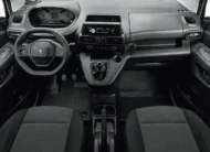 Vista interior panorámica desde la parte trasera que muestra la cabina delantera completa, el tablero ergonómico i-Cockpit, el volante, la palanca de velocidades en consola y los asientos de tela oscuros de una camioneta comercial Peugeot Partner 1.6 HDi Maxi transmisión manual año 2021 seminueva.