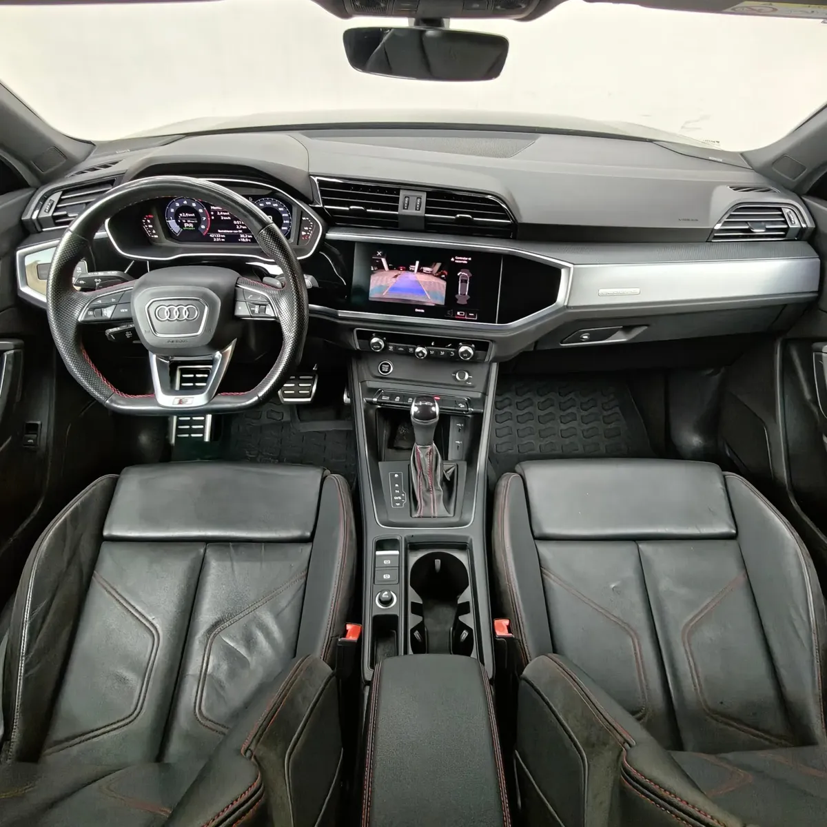 Vista interior panorámica desde la parte trasera que muestra la cabina delantera completa, el cuadro de instrumentos Audi Virtual Cockpit, la pantalla táctil de infoentretenimiento MMI con cámara de reversa, el volante deportivo multifunción S Line y los asientos deportivos en piel negra de una camioneta SUV Audi Q3 2.0 S Line 180 Hp transmisión DSG automática año 2022 seminueva.