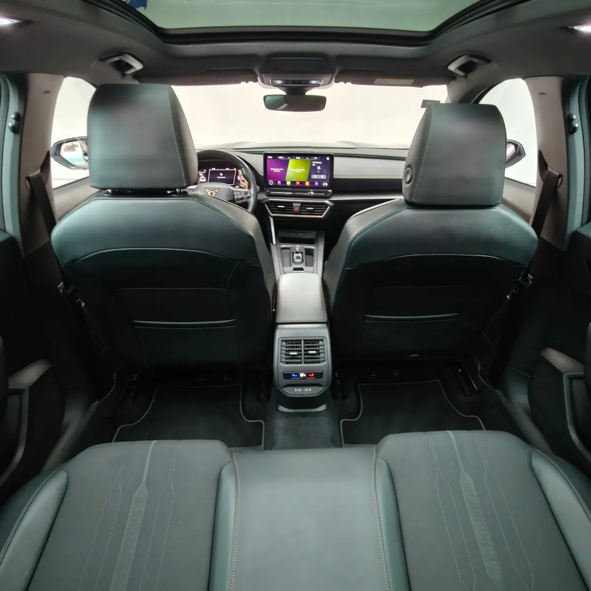 Vista interior desde los asientos traseros hacia el frente que muestra la consola posterior con salidas de aire acondicionado, los respaldos delanteros, el tablero tecnológico y el techo panorámico de una SUV Crossover deportiva Cupra Formentor 2.0 Mid 190 HP 2WD DSG7 año 2022 seminueva.