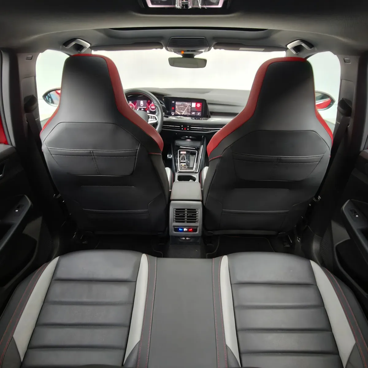 Vista interior desde la banca posterior mirando hacia el frente que muestra el respaldo de los asientos delanteros tipo bucket con acentos rojos, la consola central trasera con salidas de aire y el tablero de un hatchback deportivo Volkswagen Golf GTI 2.0 241 HP DSG7 año 2024 seminuevo.