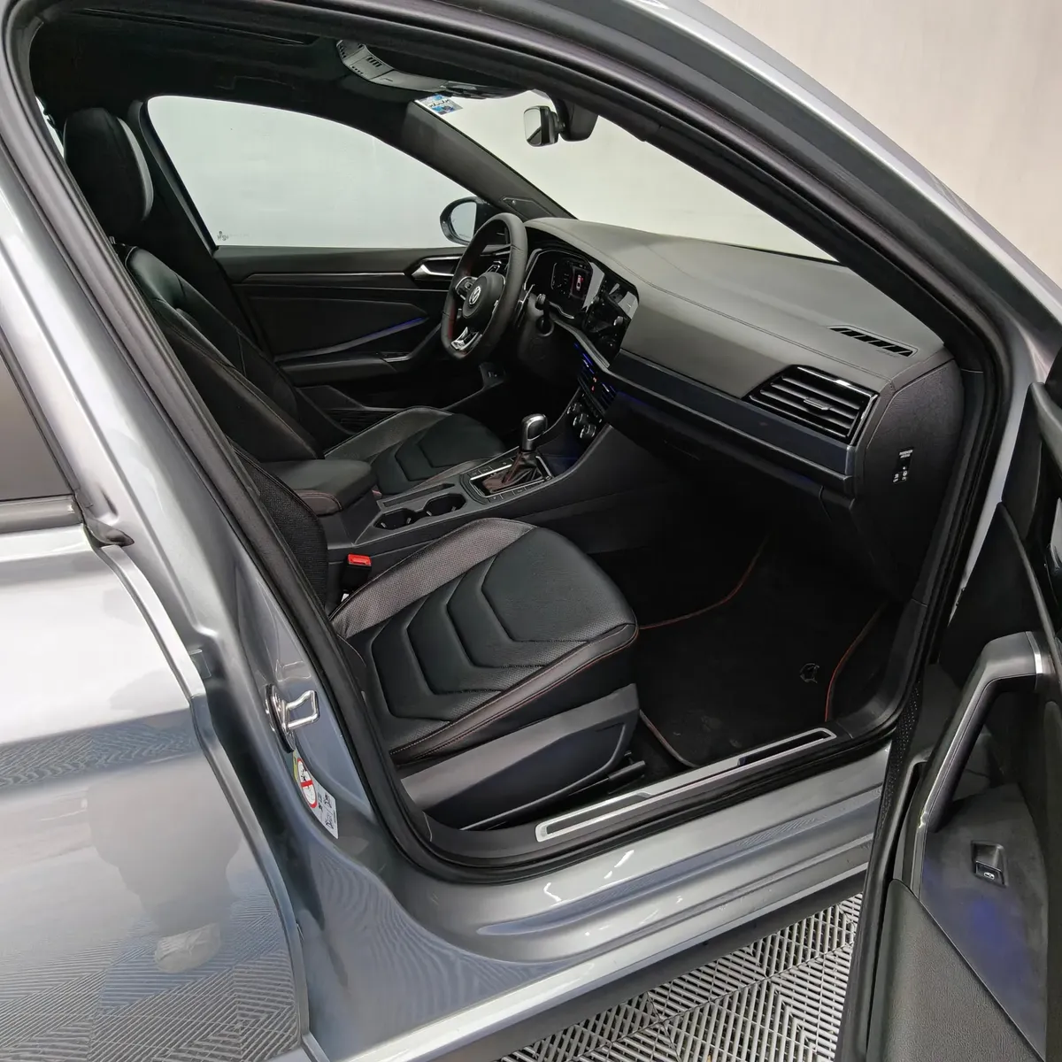 Vista interior desde la puerta del copiloto abierta que muestra los asientos deportivos de piel negra, el tablero y la consola central de un auto sedán Volkswagen Jetta 2.0 GLI DSG automático año 2021 seminuevo en ángulo oblicuo derecho.