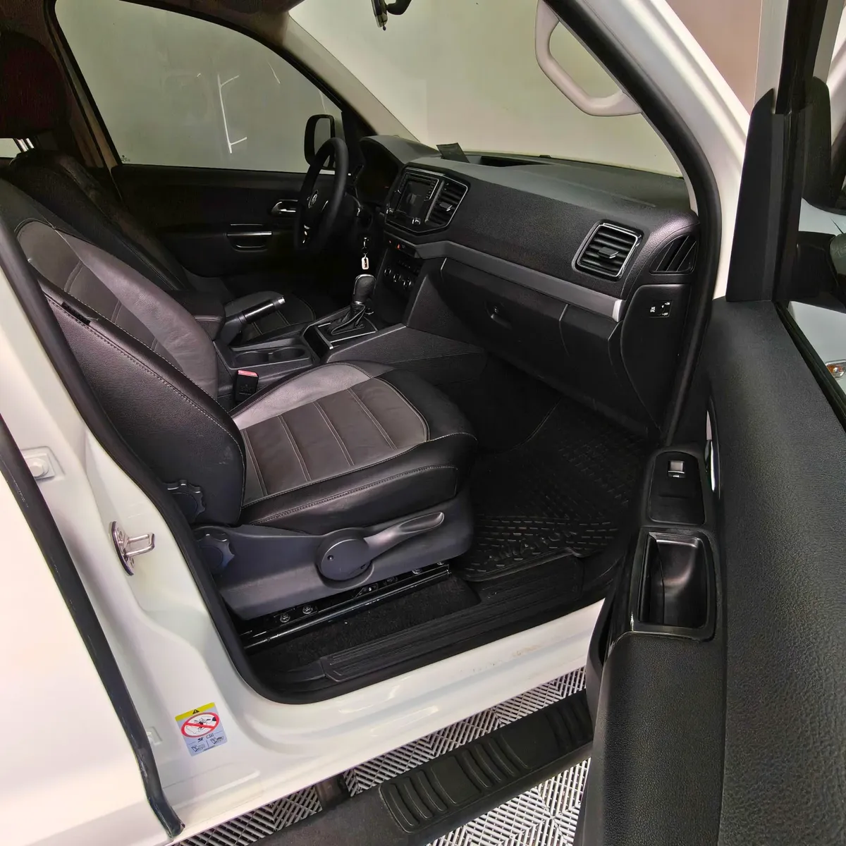 Vista interior desde la puerta del copiloto abierta que muestra el asiento de piel, la guantera, el tablero y la consola central de una camioneta pickup Volkswagen Amarok 2.0 Highline 4Motion automática año 2018 seminueva en ángulo oblicuo derecho.