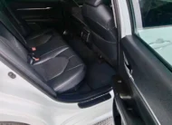 Vista interior desde la puerta trasera derecha abierta que muestra la banca de asientos posteriores en piel negra y el espacio para piernas de un auto sedán híbrido Toyota Camry 2.5 HEV XLE año 2024 seminuevo en ángulo oblicuo derecho.