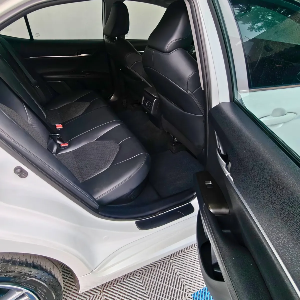 Vista interior desde la puerta trasera derecha abierta que muestra la banca de asientos posteriores en piel negra y el espacio para piernas de un auto sedán híbrido Toyota Camry 2.5 HEV XLE año 2024 seminuevo en ángulo oblicuo derecho.