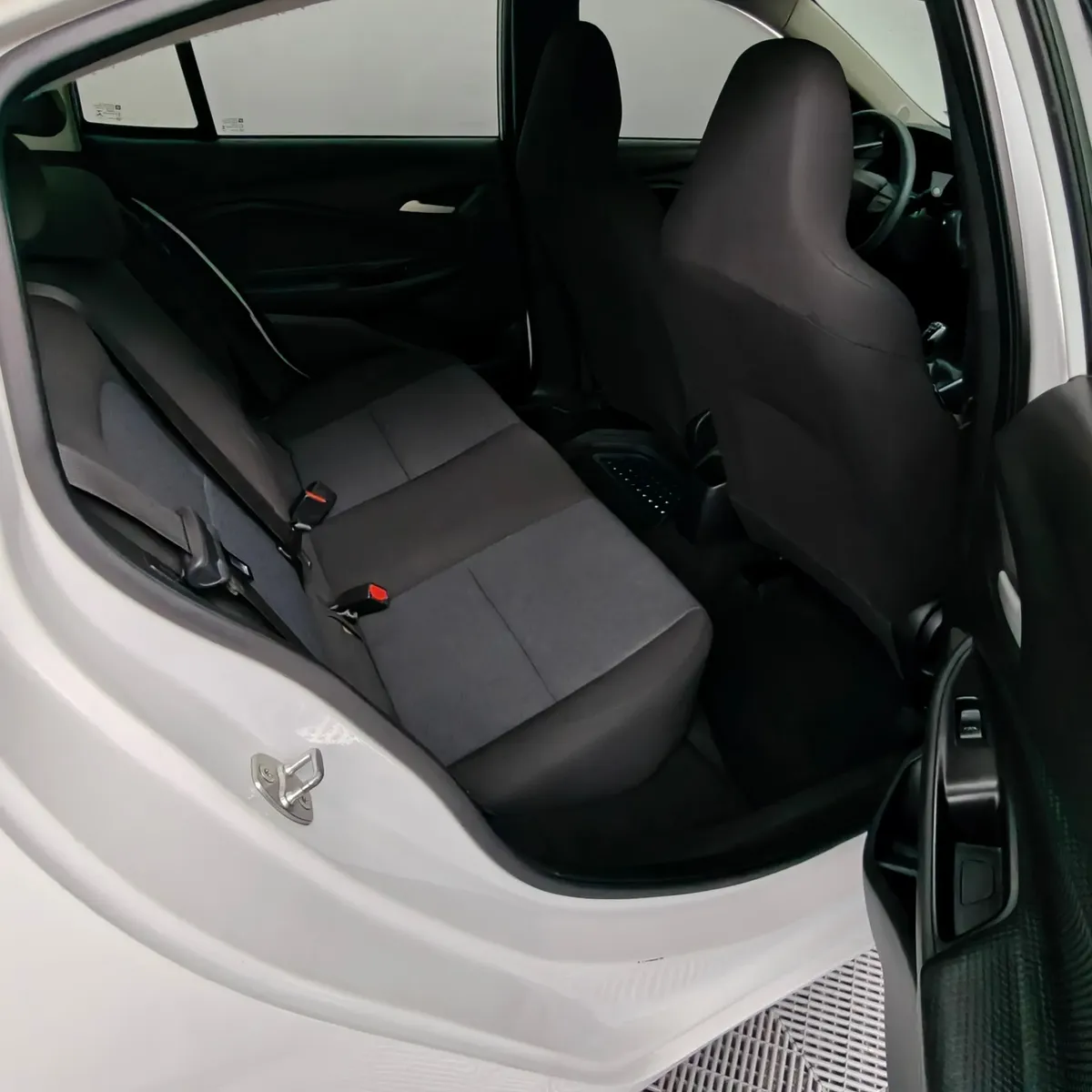 Vista interior desde la puerta trasera derecha abierta que muestra la banca de asientos posteriores en tela gris y el espacio para piernas de un auto sedán Chevrolet Onix 1.3 LS manual año 2024 seminuevo en ángulo oblicuo derecho.