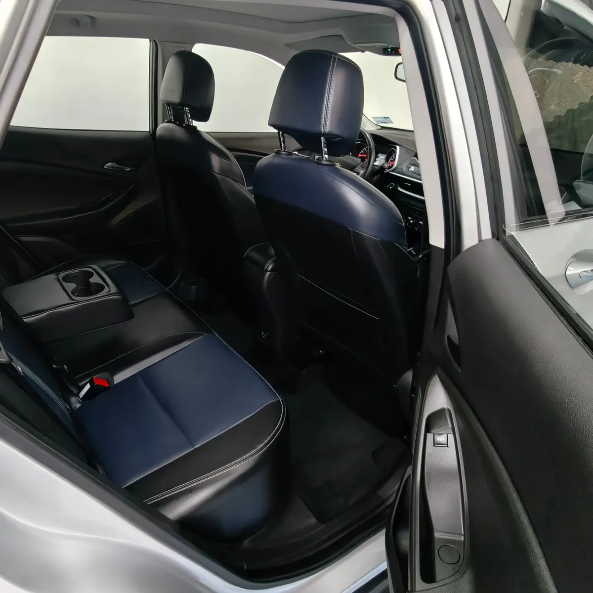 Vista interior desde la puerta trasera derecha abierta que muestra la banca de asientos posteriores tapizados en piel bitono azul y negro, el descansabrazos central desplegado con portavasos y el espacio para piernas de una camioneta SUV Chevrolet Tracker 1.2 Premier Turbo transmisión automática año 2023 seminueva en ángulo oblicuo derecho.