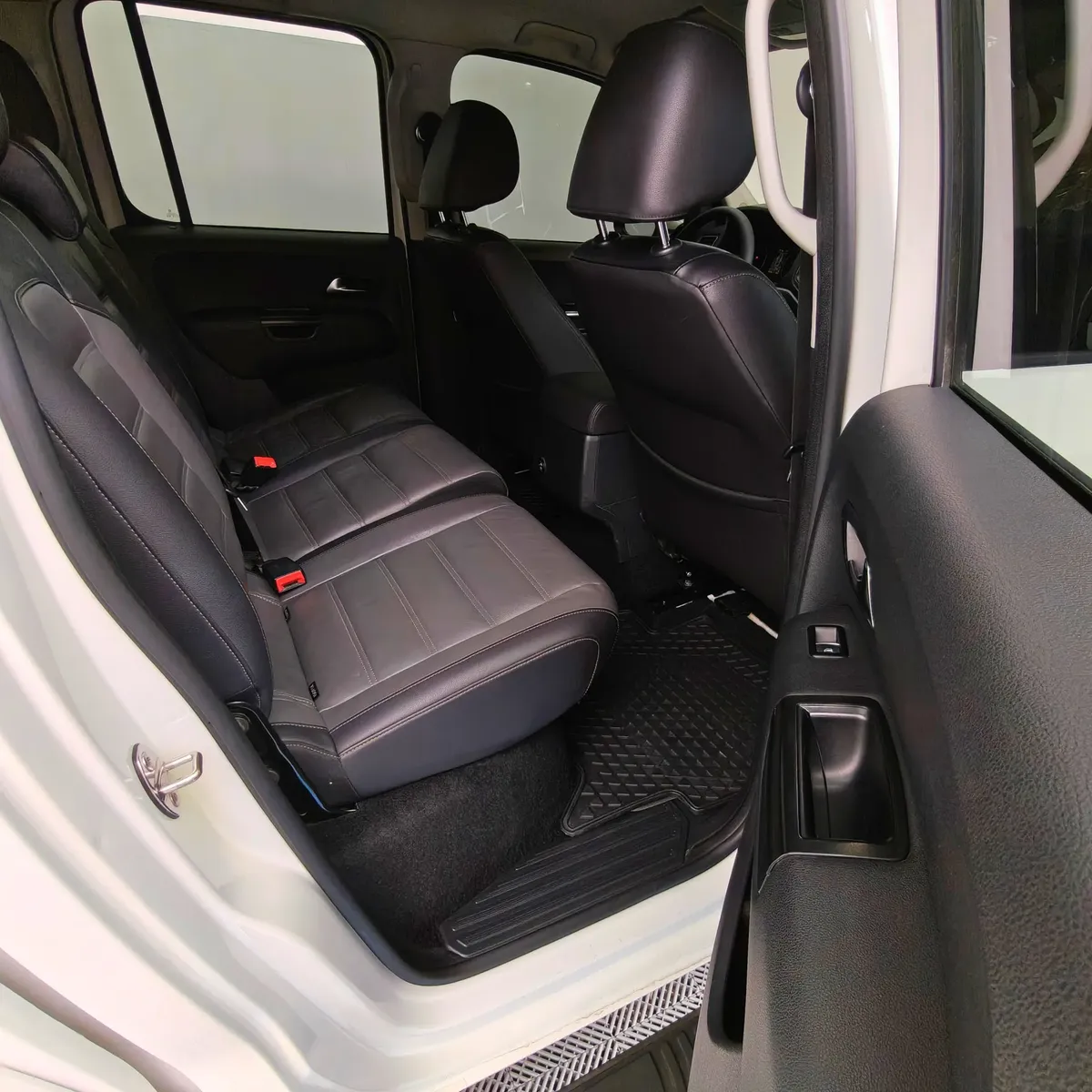 Vista interior desde la puerta trasera derecha abierta que muestra la banca de asientos posteriores tapizados en piel negra y el espacio para pasajeros de una camioneta pickup Volkswagen Amarok 2.0 Highline 4Motion automática año 2018 seminueva en ángulo oblicuo derecho.