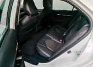 Vista interior desde la puerta trasera izquierda abierta que muestra la banca de asientos posteriores en piel negra, los respaldos delanteros y el área de pasajeros de un auto sedán híbrido Toyota Camry 2.5 HEV XLE año 2024 seminuevo en ángulo oblicuo izquierdo.