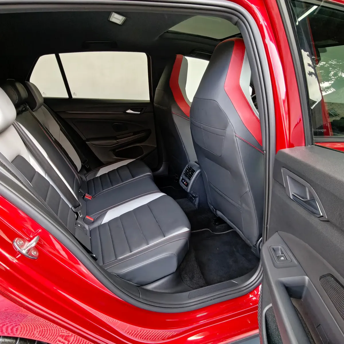 Vista interior desde la puerta trasera derecha abierta que muestra la banca de asientos posteriores bitono, el espacio para piernas, las salidas de aire acondicionado y el respaldo delantero derecho de un hatchback deportivo Volkswagen Golf GTI 2.0 241 HP DSG7 año 2024 seminuevo en ángulo oblicuo derecho.