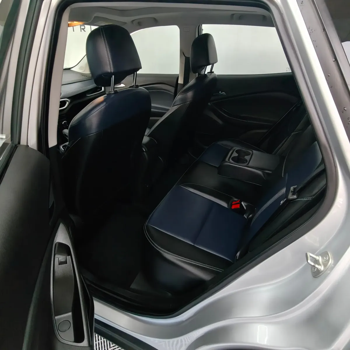 Vista interior desde la puerta trasera izquierda abierta que expone la banca de asientos posteriores tapizados en piel bitono azul y negro, el descansabrazos central abatible con portavasos y el amplio habitáculo de una camioneta SUV Chevrolet Tracker 1.2 Premier Turbo transmisión automática año 2023 seminueva en ángulo oblicuo izquierdo.