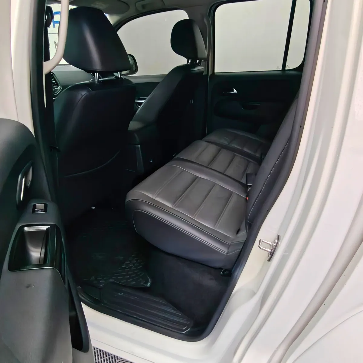 Vista interior desde la puerta trasera izquierda abierta que muestra la banca de asientos posteriores tapizados en piel negra y la zona de pasajeros de una camioneta pickup Volkswagen Amarok 2.0 Highline 4Motion automática año 2018 seminueva en ángulo oblicuo izquierdo.