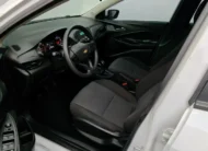 Vista interior desde la puerta del conductor abierta que muestra el asiento del piloto en tela, el volante multifunción, el cuadro de instrumentos y el tablero de un auto sedán Chevrolet Onix 1.3 LS manual año 2024 seminuevo en ángulo oblicuo izquierdo.