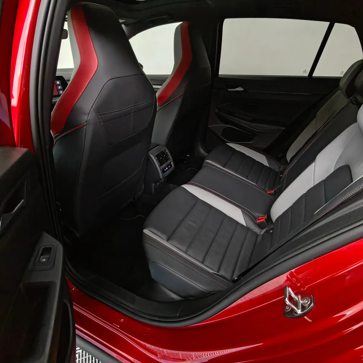 Vista interior desde la puerta trasera izquierda abierta que muestra la banca de asientos posteriores bitono, el espacio para piernas, las salidas de aire acondicionado y el respaldo del asiento del conductor de un hatchback deportivo Volkswagen Golf GTI 2.0 241 HP DSG7 año 2024 seminuevo en ángulo oblicuo izquierdo.