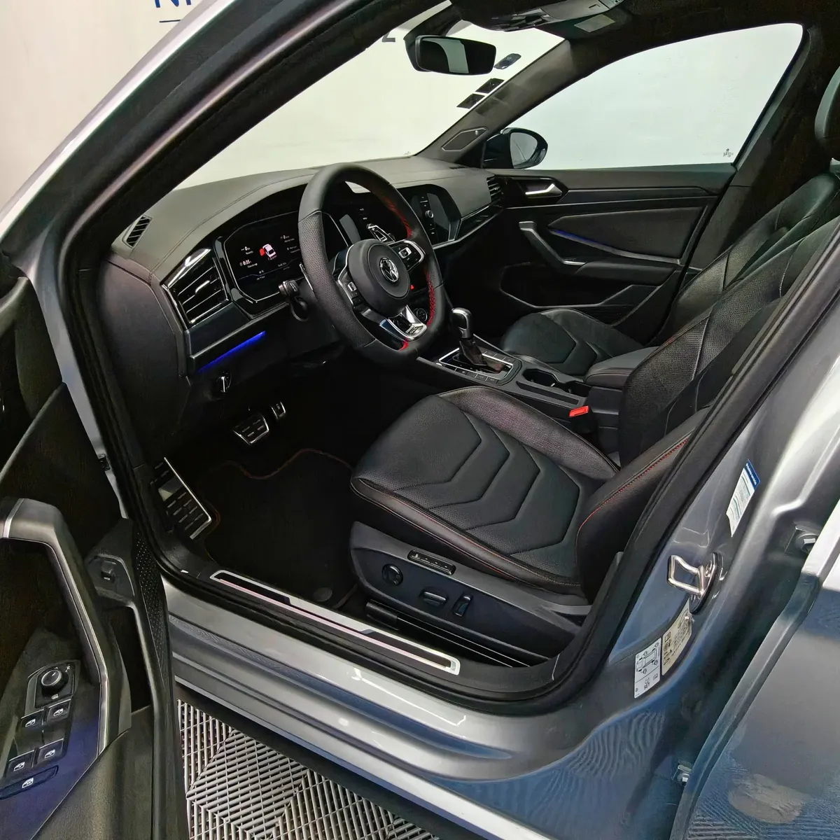 Vista interior desde la puerta del conductor abierta que muestra el asiento del piloto, volante deportivo multifunción, pedales de aluminio y tablero de un auto sedán Volkswagen Jetta 2.0 GLI DSG automático año 2021 seminuevo en ángulo oblicuo izquierdo.