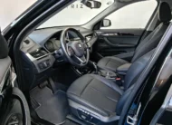 Vista interior desde la puerta del conductor abierta que muestra el puesto de mando, el asiento del piloto en piel negra con memoria y ajustes eléctricos, el volante multifunción con emblema BMW, la consola central y el tablero de una camioneta SUV de lujo BMW X1 2.0 sDrive20i sDrive 20iA X Line transmisión automática año 2022 seminueva en ángulo oblicuo izquierdo.