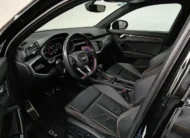 Vista interior desde la puerta del conductor abierta que muestra el puesto de mando ergonómico con volante deportivo achatado S Line, el asiento del piloto en piel negra con costuras rojas y ajustes eléctricos, pedales de aluminio y el cuadro digital Virtual Cockpit de una camioneta SUV Audi Q3 2.0 S Line 180 Hp transmisión DSG automática año 2022 seminueva en ángulo oblicuo izquierdo.