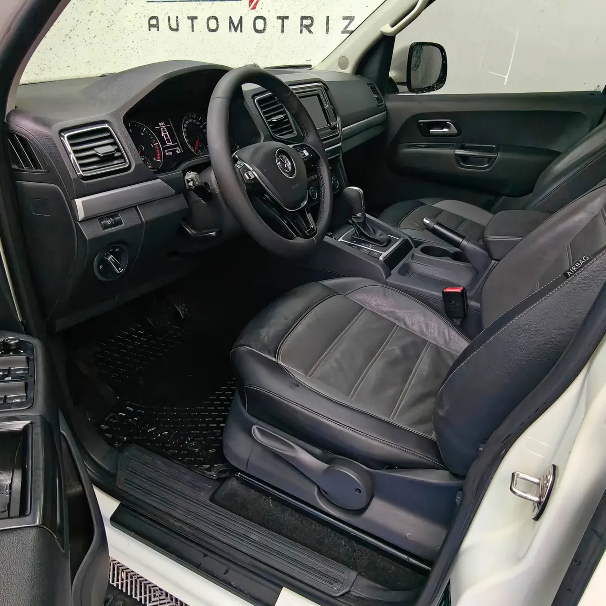 Vista interior desde la puerta del conductor abierta que muestra el asiento del piloto, volante multifunción, cuadro de instrumentos y tablero de una camioneta pickup Volkswagen Amarok 2.0 Highline 4Motion automática año 2018 seminueva en ángulo oblicuo izquierdo.