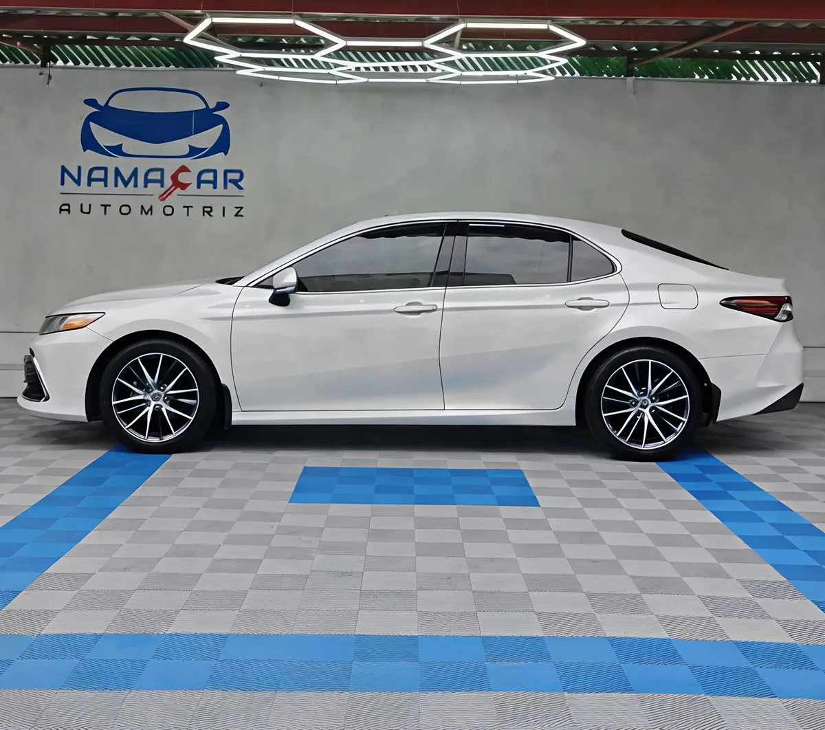 Auto sedán híbrido Toyota Camry 2.5 HEV XLE año 2024 seminuevo en color blanco, vista exterior de perfil lateral izquierdo completo exhibido en Namacar Automotriz.