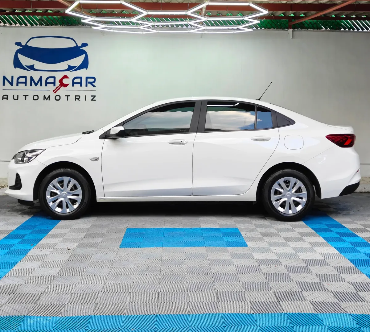 Auto sedán Chevrolet Onix 1.3 LS manual año 2024 seminuevo en color blanco, vista exterior lateral perfil izquierdo completo exhibido en Namacar Automotriz.