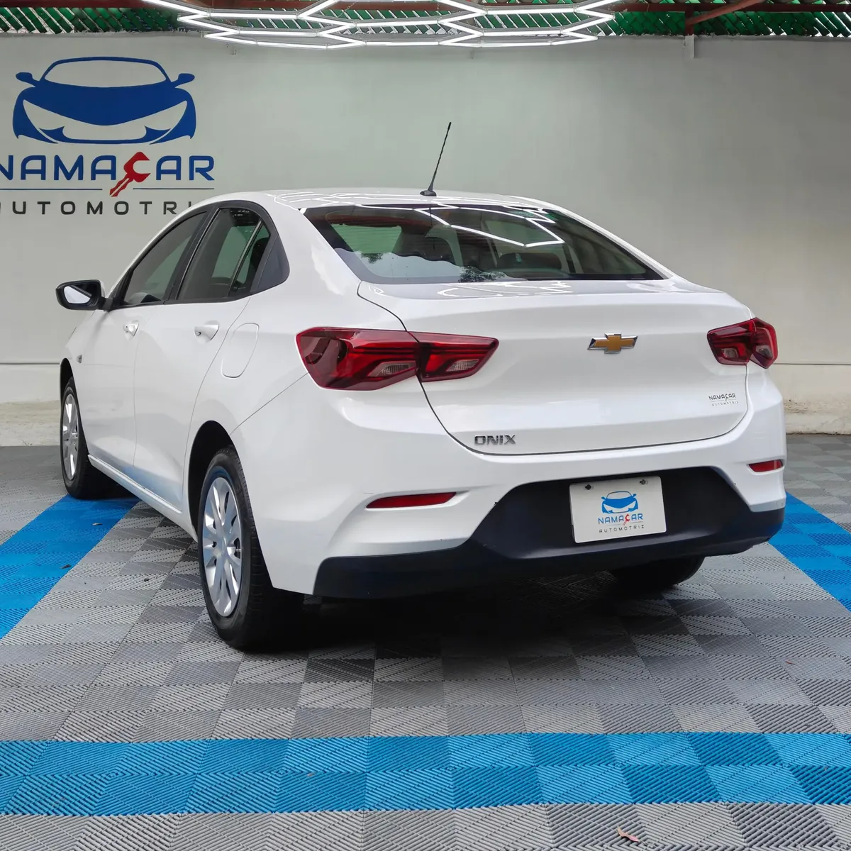 Auto sedán Chevrolet Onix 1.3 LS manual año 2024 seminuevo en color blanco, vista exterior trasera en ángulo de tres cuartos izquierda exhibido en Namacar Automotriz.