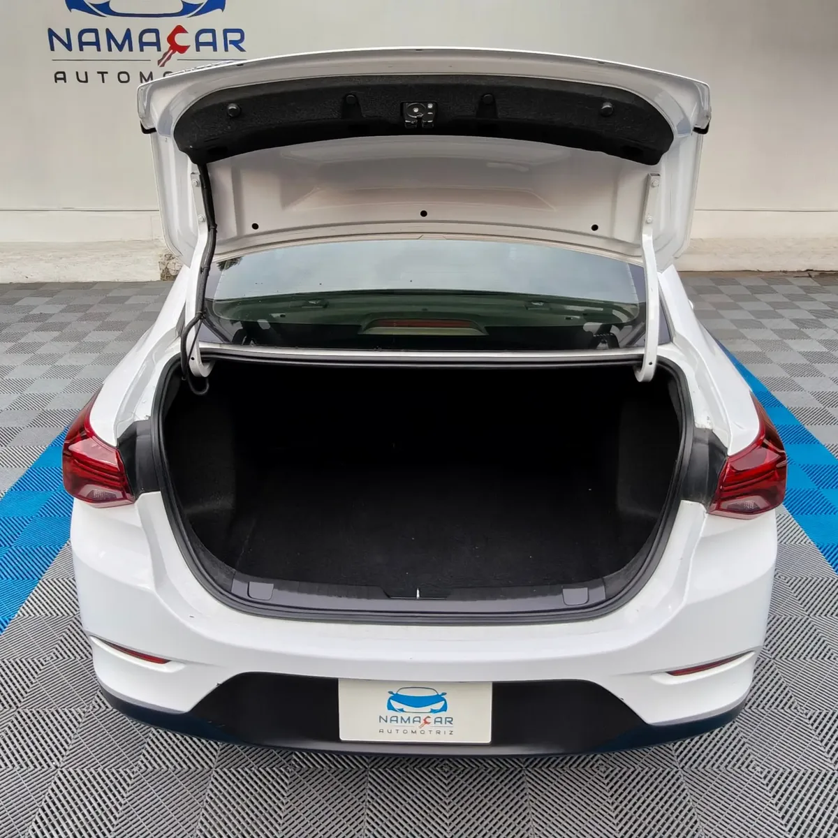 Auto sedán Chevrolet Onix 1.3 LS manual año 2024 seminuevo en color blanco, vista exterior trasera centrada con la cajuela abierta mostrando el compartimento de carga.