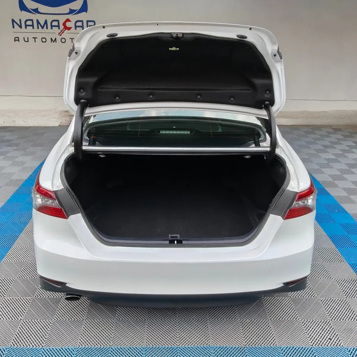 Vista exterior trasera directa con la cajuela abierta que muestra el amplio espacio del compartimento de equipaje de un auto sedán híbrido Toyota Camry 2.5 HEV XLE año 2024 seminuevo en color blanco, en Namacar Automotriz.