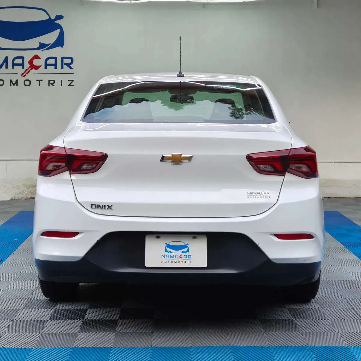 Auto sedán Chevrolet Onix 1.3 LS manual año 2024 seminuevo en color blanco, vista exterior trasera directa y centrada exhibido en Namacar Automotriz.