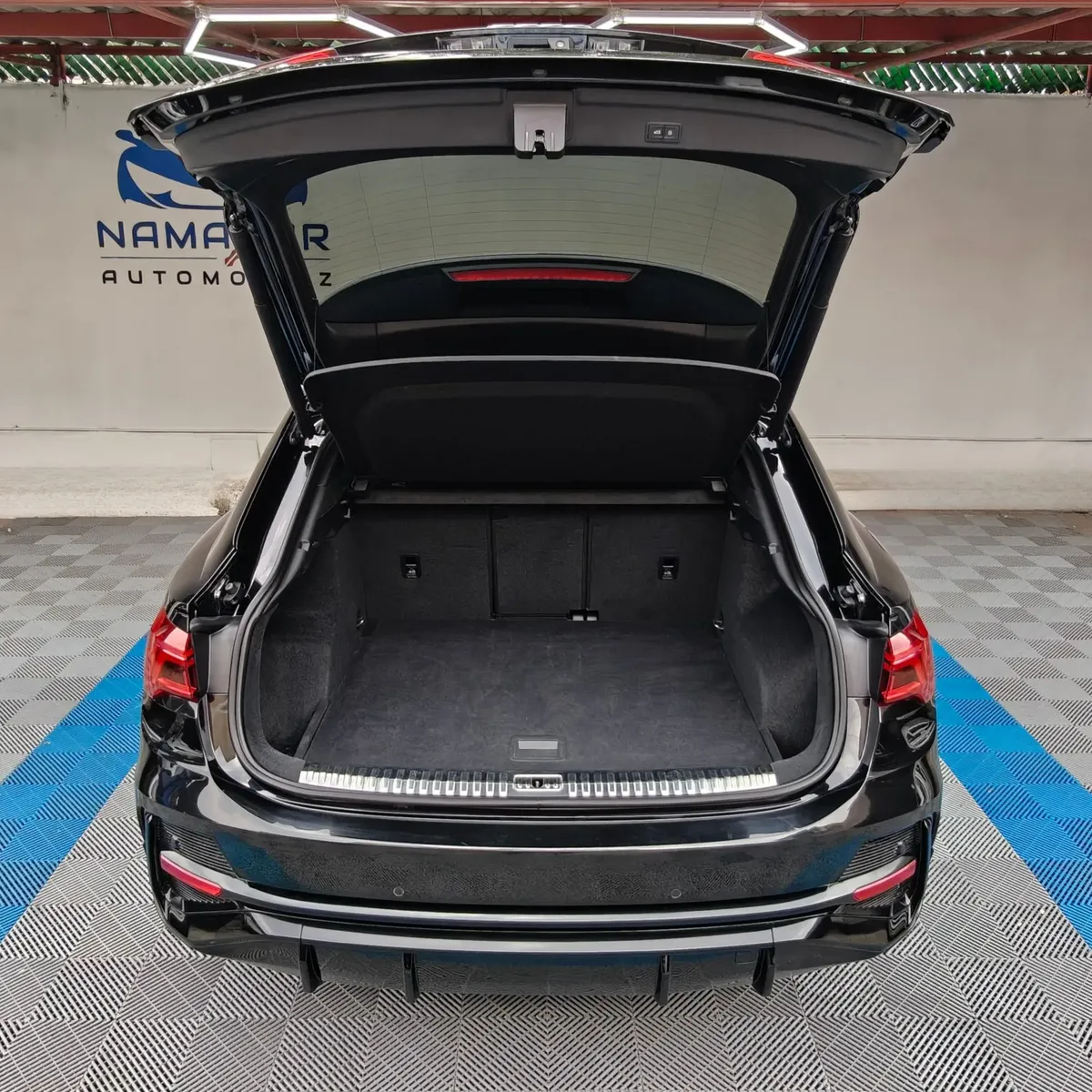 Camioneta SUV coupé de lujo Audi Q3 Sportback 2.0 S Line 180 Hp transmisión DSG automática año 2022 seminueva en color negro, vista exterior trasera centrada con el cajuela abierta mostrando el amplio maletero en Namacar Automotriz.