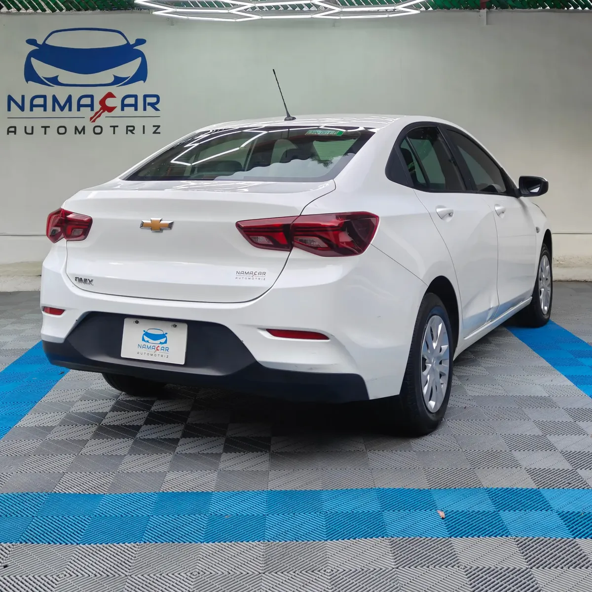 Auto sedán Chevrolet Onix 1.3 LS manual año 2024 seminuevo en color blanco, vista exterior trasera en ángulo de tres cuartos derecha exhibido en Namacar Automotriz.