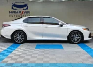 Auto sedán híbrido Toyota Camry 2.5 HEV XLE año 2024 seminuevo en color blanco, vista exterior de perfil lateral derecho completo exhibido en Namacar Automotriz.